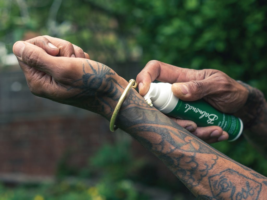 Applying vegan aftercare lotion to a tattooed arm